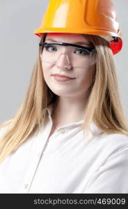 Portrait of a young attractive woman with blond hair in orange helmet and glasses on a neutral gray background.. Portrait of a young attractive woman with blond hair in orange helmet on a neutral gray background.