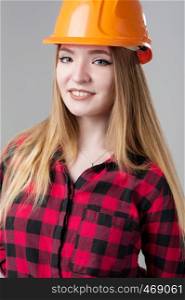 Portrait of a young attractive woman with blond hair in orange helmet and in a plaid shirt on a neutral gray background.. Portrait of a young attractive woman with blond hair in orange helmet on a neutral gray background.