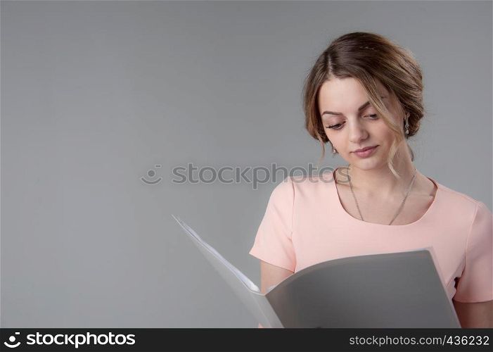 Portrait of a young attractive woman with blond hair on a neutral gray background. Gray folder in hand.. Portrait of a young attractive woman with blond hair on a neutral gray background.