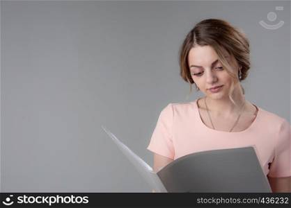 Portrait of a young attractive woman with blond hair on a neutral gray background. Gray folder in hand.. Portrait of a young attractive woman with blond hair on a neutral gray background.