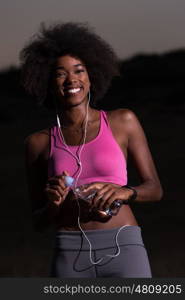 portrait of a young beautiful african american woman with headphones and a bottle of water after jogging in nature beautiful summer night