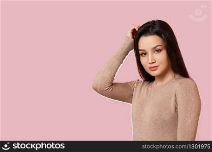 portrait of a young beautiful Asian brunette girl in a light brown jacket holding her head with her hands . on a pink isolated background with copyspace.