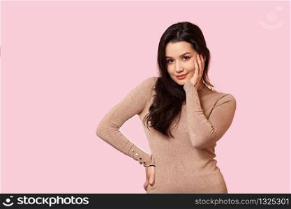 portrait of a young beautiful Asian brunette girl in a light brown jacket holding her hands over her face . on a pink isolated background with copyspace.