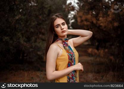 portrait of a young beautiful girl in a yellow dress with a colorful scarf standing in the woods