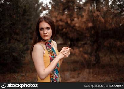 portrait of a young beautiful girl in a yellow dress with a colorful scarf standing in the woods