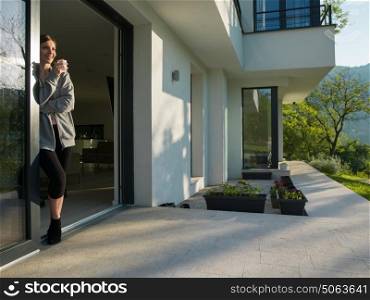 portrait of a young beautiful successful woman drinking coffee in the doorway of her luxury home villa