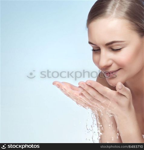 Portrait of a young beautiful woman cleaning her face by water, isolated on blue background, morning freshness, removing makeup, skin health and beauty care concept. Skin care routine