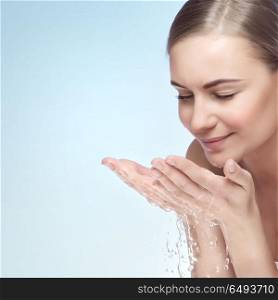 Portrait of a young beautiful woman cleaning her face by water, isolated on blue background, morning freshness, removing makeup, skin health and beauty care concept. Skin care routine