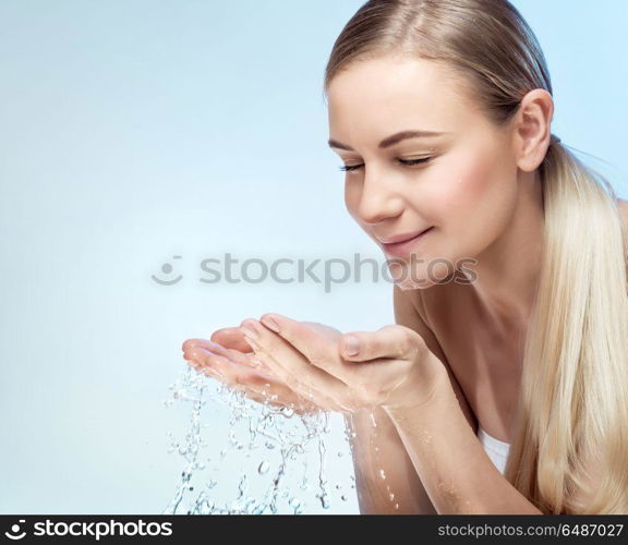 Portrait of a young beautiful woman cleaning her face with fresh cold water, isolated on blue background, morning freshness, removing makeup, health and beauty care concept. Fresh morning start