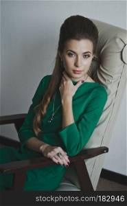 Portrait of a young beauty in a green chair.. Girl in green dress sitting in a chair 4874.