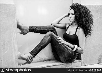 Portrait of a young black woman, afro hairstyle, wearing blue jeans in urban background