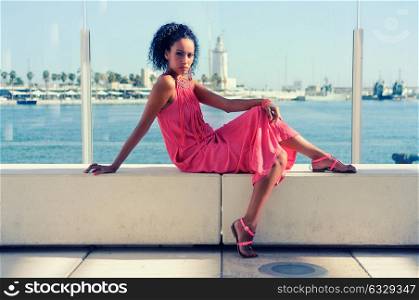 Portrait of a young black woman, afro hairstyle, wearing long pink dress, in the harbour