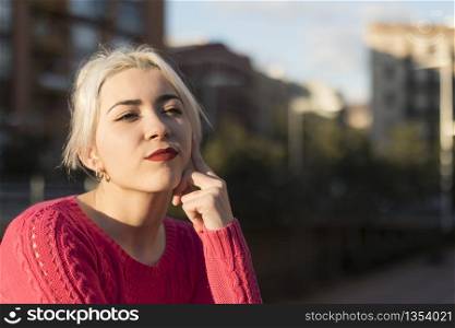 Portrait of a young blonde woman gesturing in the street wearing a red sweeter