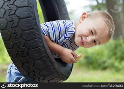 Portrait of a young boy winking while swinging on tire