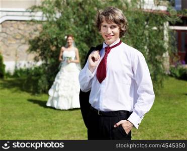 Portrait of a young bride in nature in a dark suit and red tie