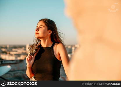 portrait of a young brunette girl in black sneakers,black shorts and a black short top standing on the roof and enjoying the sunset