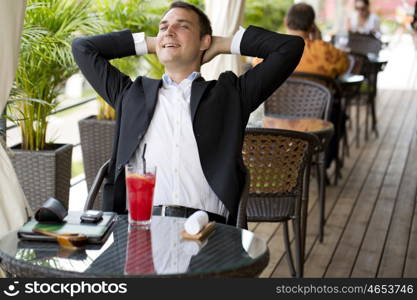 Portrait of a young business man in a dark suit and white shirt sitting in summer cafe