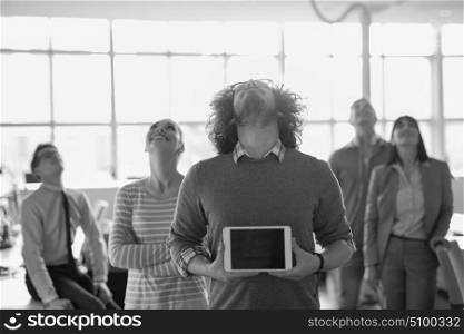 Portrait of a young businessman holding tablet in bright office with colleagues in the background