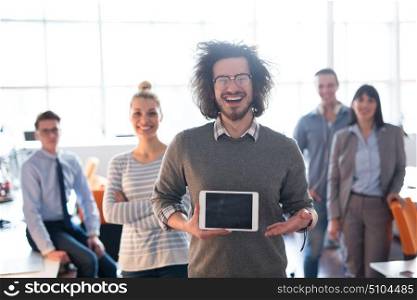 Portrait of a young businessman holding tablet in bright office with colleagues in the background