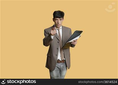 Portrait of a young businessman pointing while holding clipboard over colored background