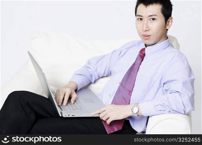 Portrait of a young businessman sitting in an armchair and using a laptop