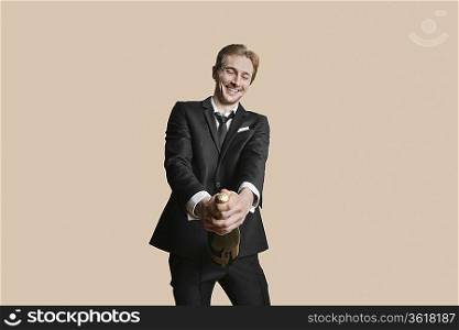 Portrait of a young businessman uncorking champagne over colored background