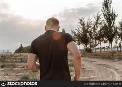 portrait of a young Caucasian guy in a black t-shirt and black shorts running over rough terrain during sunset