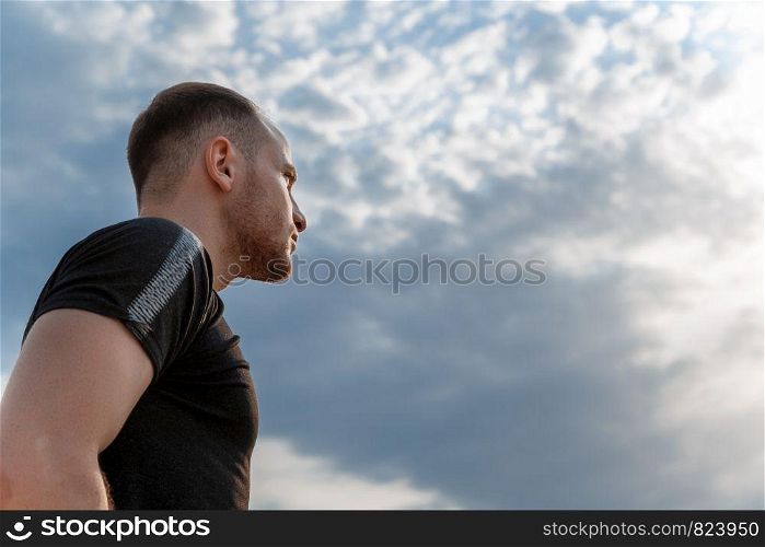 portrait of a young Caucasian guy in a black t-shirt and black shorts running at sunset