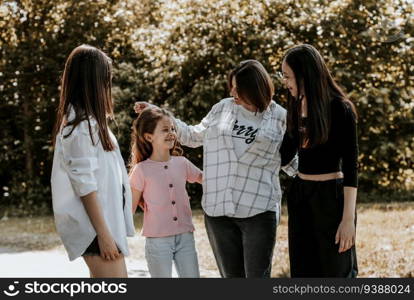 Portrait of a young Caucasian mother with her three adult daughters chatting and having fun in a city park on a summer day, close-up view from the side.. Portrait of a young mother with her three daughters in the park.
