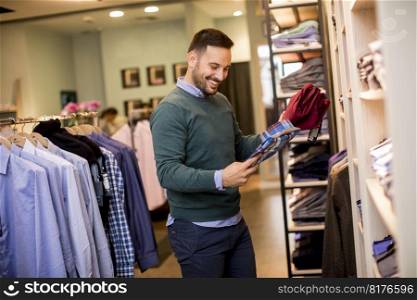 Portrait of a young cheerfull man looking at clothes to buy at shop