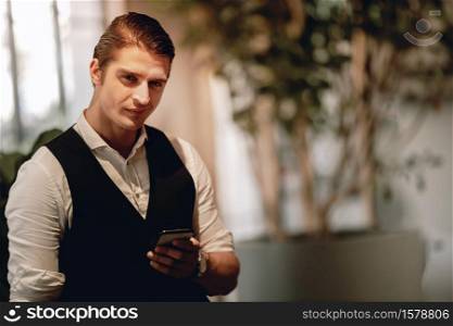 Portrait of a Young Confident CEO or Leader in the Modern Workplace. Confident Caucasian Businessman using Mobile Phone. Looking at Camera