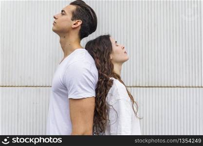 Portrait of a young couple back to back on a white wall