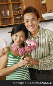 Portrait of a young couple holding a flower vase in the kitchen