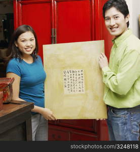 Portrait of a young couple holding a painting and smiling
