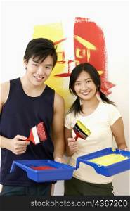 Portrait of a young couple holding paintbrushes with paint trays and smiling