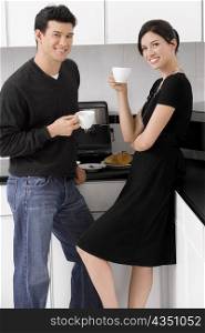 Portrait of a young couple holding their coffee cups in the kitchen and smiling