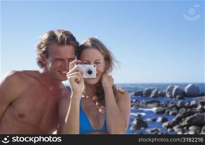 Portrait of a young couple looking through a camera on the beach