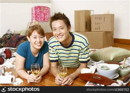 Portrait of a young couple lying on the floor and holding glasses of wine