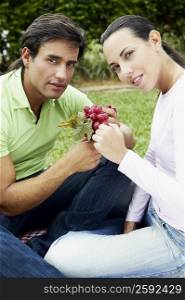Portrait of a young couple sitting and holding a bunch of grapes