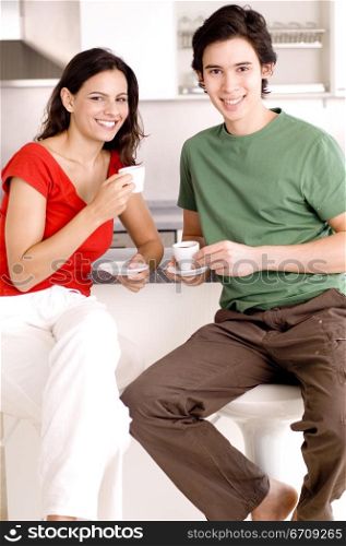 Portrait of a young couple sitting in a kitchen and holding cups of tea