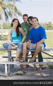 Portrait of a young couple sitting on a picnic table with another young couple standing in the background