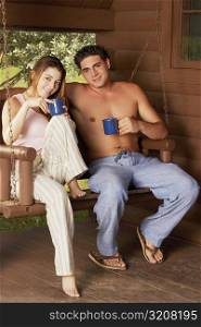 Portrait of a young couple sitting on a porch swing and holding cups of tea