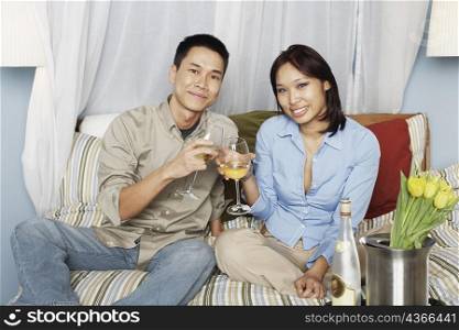 Portrait of a young couple sitting on the bed toasting with wineglasses
