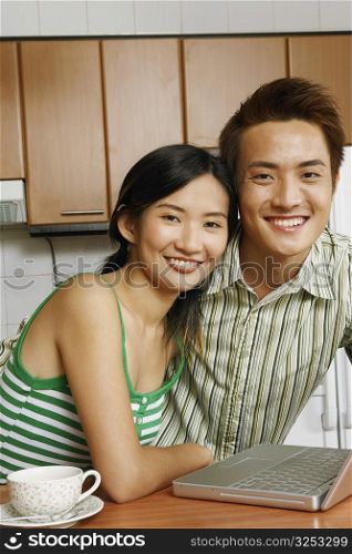 Portrait of a young couple smiling in front of a laptop at a kitchen counter