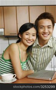 Portrait of a young couple smiling in front of a laptop at a kitchen counter
