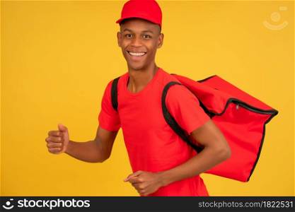 Portrait of a young delivery man looking at the camera and showing thumb up while standing against isolated yellow background. Delivery service concept.