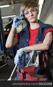 Portrait of a young female mechanic wearing protective eyewear in garage