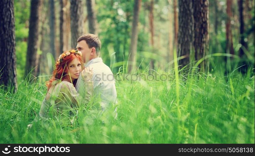 Portrait of a young gentle couple sitting on a fresh green grass in the forest, hugging and enjoying spending time together