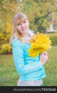 Portrait of a young girl with bouquet of yellow maple leaf in the autumn nature close-up