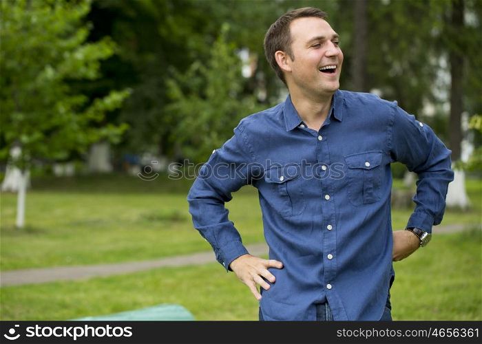 Portrait of a young handsome man in a blue shirt on the background of summer park